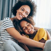 Lovely mother embracing her cute daughter on the sofa at home.